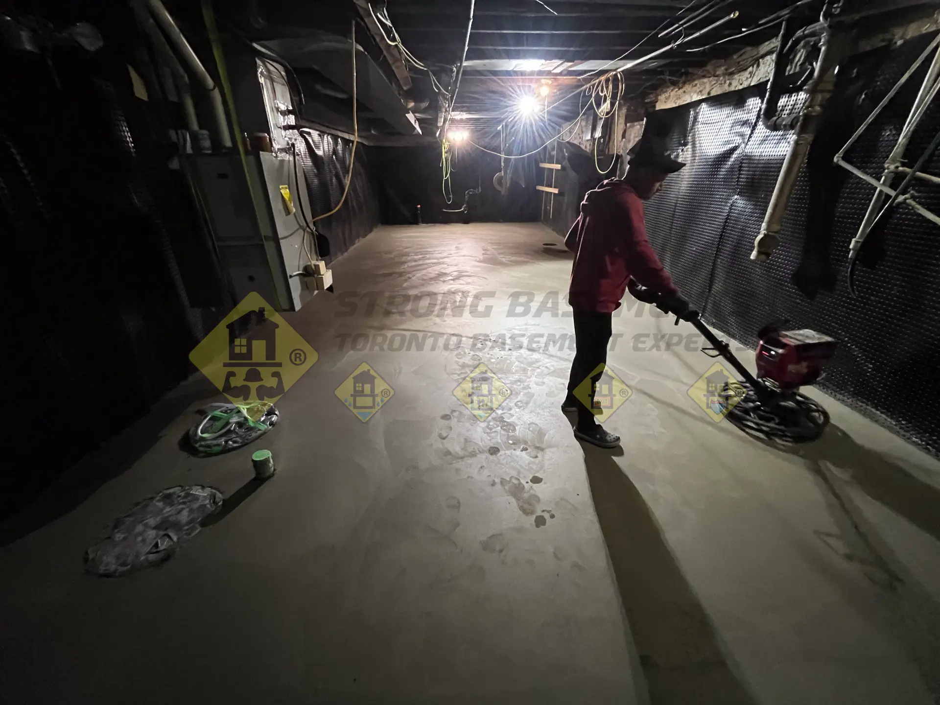 A concrete professional uses a powered trowel to finish a freshly poured concrete slab, creating a smooth, even surface for a newly lowered basement in Leaside, Toronto.